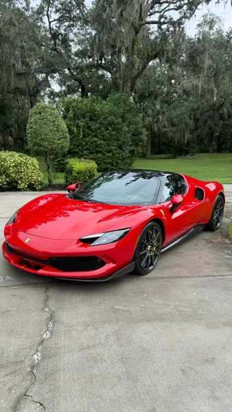 Red Ferrari 296 with a glossy finish parked on a driveway under oak trees